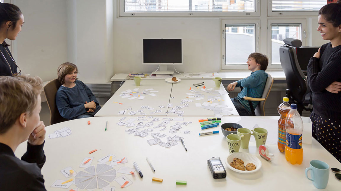 Workshop setup depicting three teenagers sitting around a table placing paper pieces together to form pie charts of their money spending habit