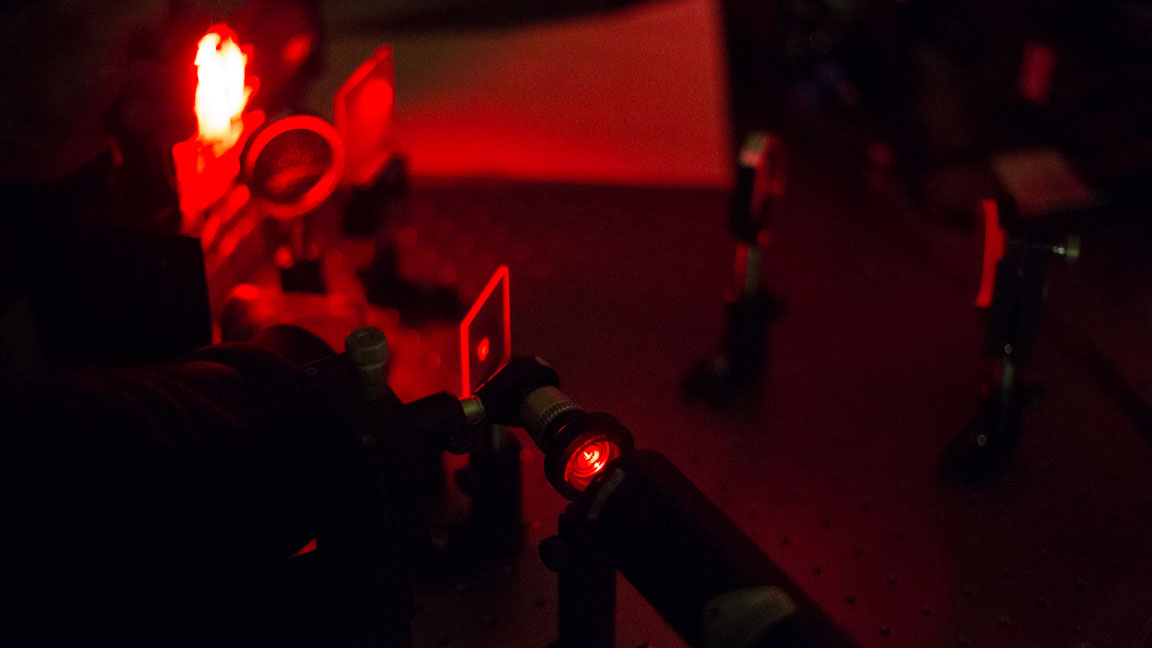Laser shooting red laser light, illuminating a metal table and a paper setup