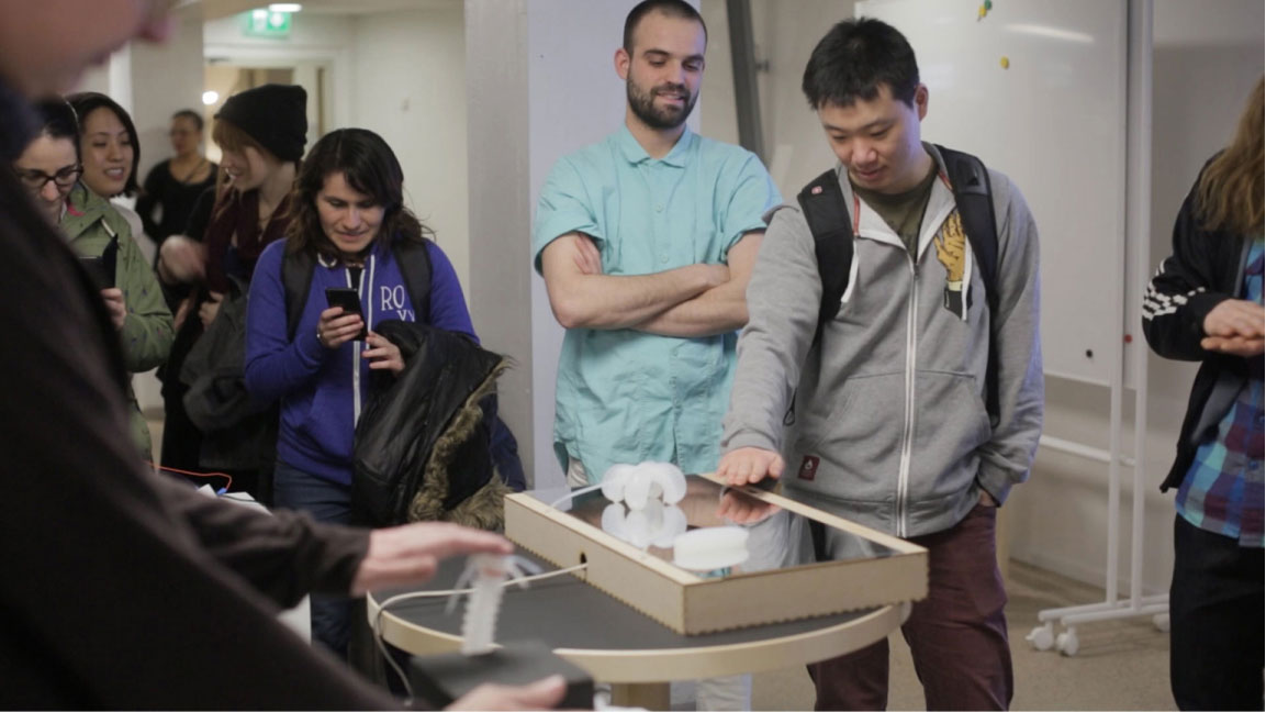 People standing around a table showing a small silicone tube which expands and moves