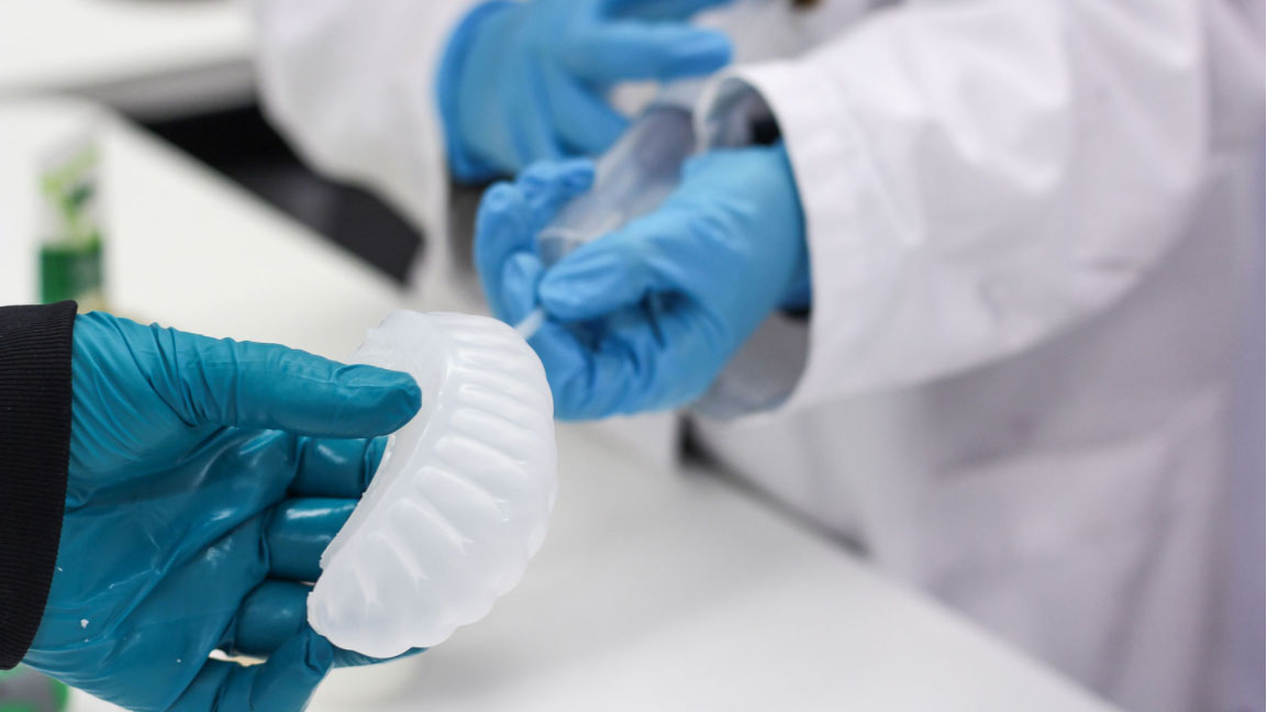 Two glove covered pairs of hands holding an air filled silicone actuator