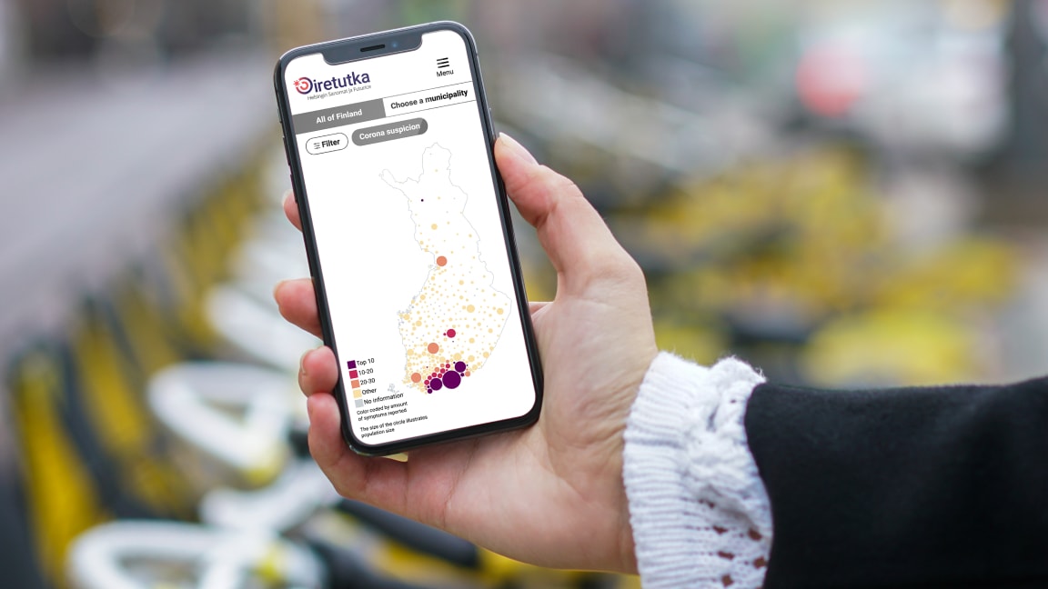Person holding a phone showing a map of Finland overlayed with differently sized circles representing the amount of suspected Corona cases